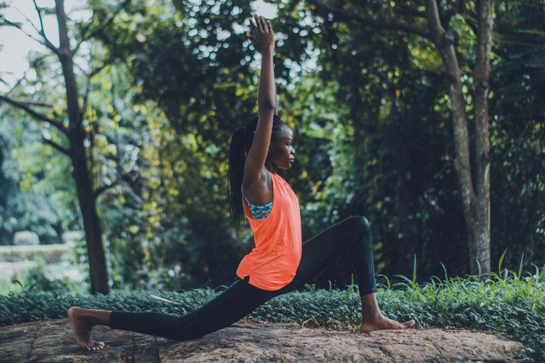 photo of woman in orange tank top and black pants striking a yoga pose outdoors